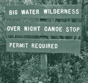 A sign in the woods that says Big Water Wilderness Over Night Canoe Stop Permis Required