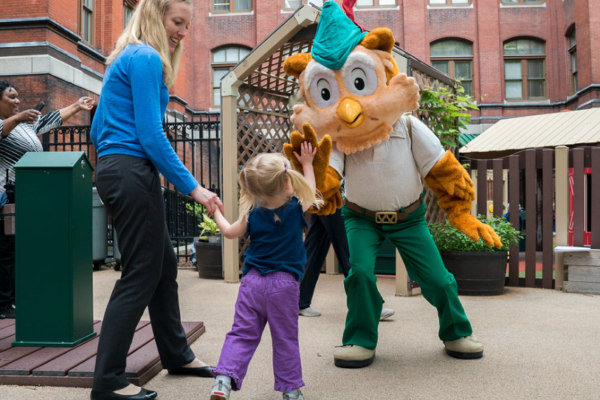 Woodsy gives a small child a high five while her mother looks on