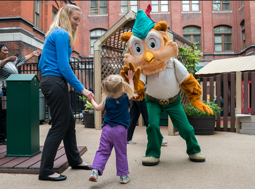 Woodsy gives a small child a high five while her mother looks on